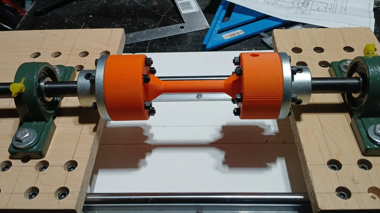 Fabricated torsion testing prototype with an orange specimen fixture supported between shaft bearings